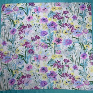 May include: A square floral scarf with a white background and a colorful pattern of purple, pink, yellow, and blue flowers. The scarf has a teal border and a delicate, feminine design. The flowers are detailed and arranged in a naturalistic style.