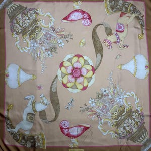 May include: A square silk scarf with a tan background and a brown border. The scarf features ornate vases, flowers, and stylized horses in shades of beige, pink, and gold. A large floral design is in the center.