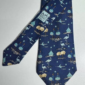 Pode incluir: Gravata de seda azul marinho com um padrão repetido de bateristas, árvores, pássaros, estrelas e luas crescentes. A gravata apresenta o logotipo "Hermès Paris". O design é em tons de azul, bege e branco.