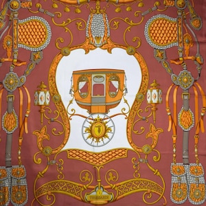 May include: A silk scarf with a detailed carriage design in shades of orange, gold, and gray on a burgundy background. The scarf features ornate decorative elements and the brand name "TRUSSARDI".