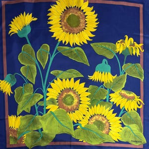 May include: A square, navy blue scarf featuring a vibrant sunflower design. The sunflowers are yellow with brown centers and green leaves. The scarf has a brown border and the word "TORRENTE" is visible in the bottom right corner.