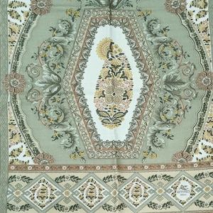 May include: A detailed textile with a repeating floral pattern in shades of green, beige, and brown. The central design features a floral motif within an oval frame. The overall design is symmetrical and ornate, suitable for home decor.