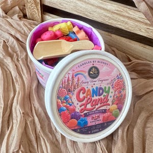 Op de afbeelding: Een witte ronde container gevuld met kleurrijke waxmelts en een klein houten schepje. Het deksel heeft een label met de tekst CANDLES BY BLONDY, Luxury Home Fragrance, CANDY Land, WAX MELTS, CHUCHES en 100G, met een afbeelding van een kasteel.
