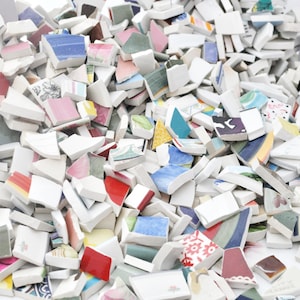 May include: A pile of broken ceramic pieces with various colors and patterns. The fragments include white, red, blue, green, and pink hues, with floral and geometric designs. The pieces vary in size and shape, creating a mosaic effect.