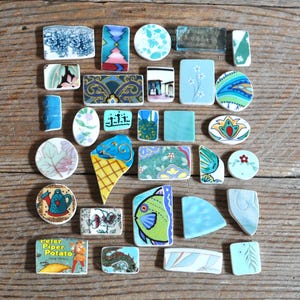 May include: A collection of assorted ceramic and glass mosaic tiles in various shapes and sizes. The pieces feature diverse patterns including floral motifs, geometric designs, a fish illustration, an ice cream cone, and a Peter Piper Potato label.