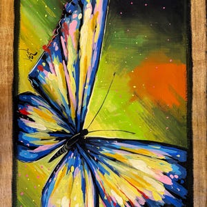 May include: Colorful butterfly painting with blue, yellow, pink, and red wings against a green and orange background. The artwork is framed in a wooden border, showcasing a vibrant and artistic depiction of the insect.