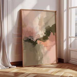 May include: Abstract art print in a gold frame. The artwork features a blend of colors, including pink, olive green, and beige, with brushstroke textures. The framed art is leaning against a white wall next to a window.