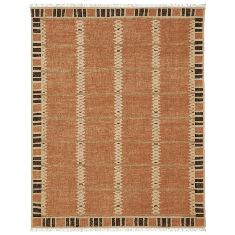May include: A rectangular woven rug in shades of orange, beige, and brown. The rug has a repeating geometric pattern of vertical lines and rectangular blocks. The edges are finished with a fringe.
