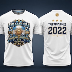 Puede incluir: Camiseta blanca con un diseño que celebra las victorias de Argentina en la Copa del Mundo. El frente muestra "¡VAMOS ARGENTINA!" con los años 1978, 1986 y "TRICAMPEONES 2022." La parte trasera tiene "TRICAMPEONES 2022" y un emblema de sol.