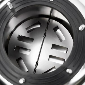 May include: A circular stainless steel chamber featuring a central hinged plate with rectangular cutouts. The interior is surrounded by a thick black rubber gasket secured with metal fasteners, creating a mechanical industrial appearance.