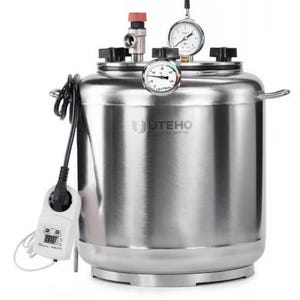 May include: A stainless steel autoclave with a cylindrical body, featuring a top lid secured by black knobs. It includes a pressure gauge, a temperature gauge, a red valve, and a digital controller with a power cord attached to the side.