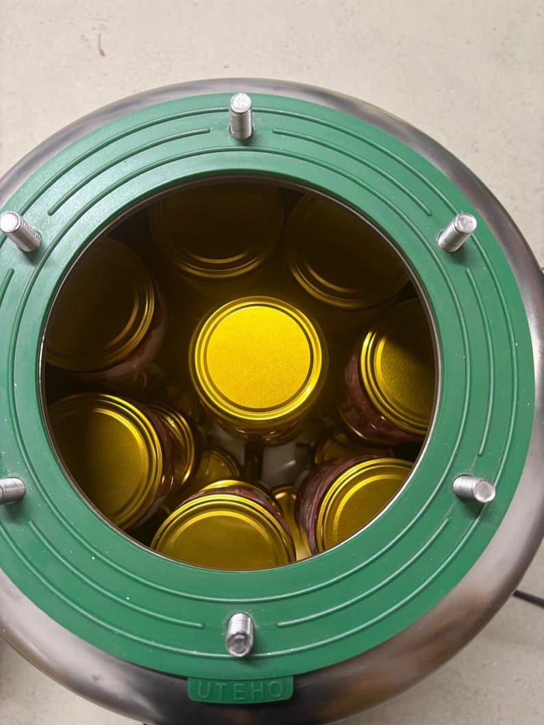 May include: A stainless steel canning or processing device with a circular green gasket featuring four protruding metal bolts. Inside the device, multiple glass jars with bright gold lids are arranged in a circular pattern. The word UTEHO is embossed on the green rim.