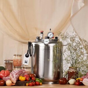 May include: A stainless steel pressure canner with a digital temperature controller, two analogue pressure gauges, and a red valve on top. The unit is surrounded by fresh produce including tomatoes, onions, aubergine, courgette, and raw meat in jars.