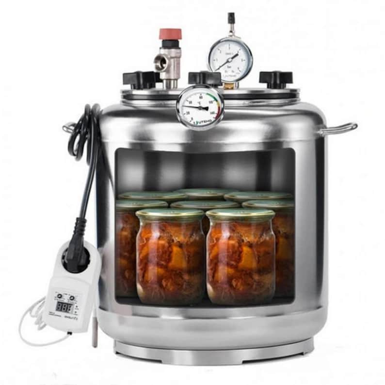 May include: A stainless steel pressure canner with a large rectangular viewing window showing glass jars filled with food inside. The lid features a pressure gauge, a thermometer, and a red valve. A white digital power controller is attached by a cord.