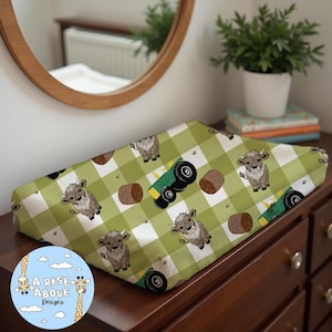 May include: A green and white checkered changing pad cover with a repeating pattern of cartoon cows, tractors, and hay bales. The changing pad cover is made of soft, comfortable fabric and is perfect for protecting your changing pad from spills and messes.