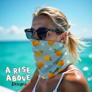 May include: A light blue face covering with a pattern of oranges and white flowers. The text "A Rise Above Designs" is visible in the lower left corner. The face covering is being worn by a person wearing sunglasses.