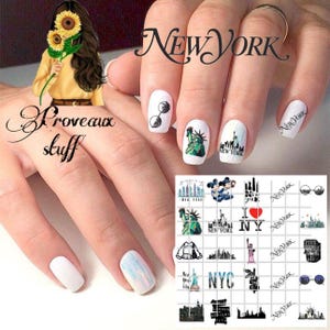 May include: White nail art with New York City themed designs. The nails feature images of the Statue of Liberty, sunglasses, and the city skyline. The word "New York" is also displayed on the nails.