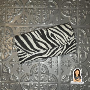 May include: A rectangular clutch wallet featuring a bold black and white zebra stripe pattern. The wallet has a fold-over flap closure design with a consistent striped print across the entire exterior surface, creating a high-contrast visual effect.