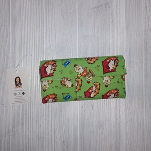 May include: A green fabric wallet with a repeating pattern of cartoon chickens. The chickens are red, yellow, and brown with black eyes. The wallet is folded closed and has a flap with a snap closure.