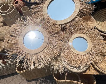 May include: A display of handcrafted mirrors with a sunburst design, featuring a round mirror surrounded by natural-colored straw. Woven baskets and decorative plates in various colors and patterns are also visible, creating a rustic, bohemian aesthetic.