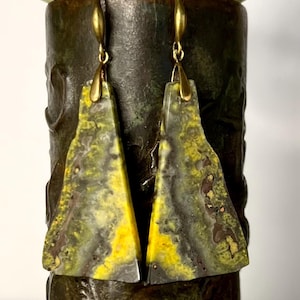May include: A pair of yellow, green, and brown earrings with gold-toned hooks. The earrings are made of resin and have a unique, abstract design.