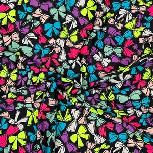 Könnte beinhalten: Ein Stoff mit einem sich wiederholenden Muster aus bunten Schleifen in Pink-, Grün-, Blau-, Lila- und Weißtönen auf schwarzem Hintergrund. Die Schleifen sind in verschiedenen Größen und Ausrichtungen angeordnet und erzeugen ein lebendiges Design.