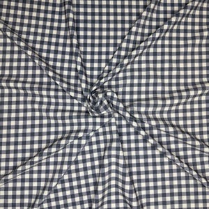 Op de afbeelding: Een close-up van een witte en zwarte gingham stof met een geruit patroon. De stof is gevouwen en gekreukt, waardoor een textuur ontstaat.