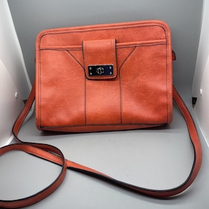 May include: A bright orange crossbody bag with a flap closure and a silver buckle. The bag has a long adjustable strap.
