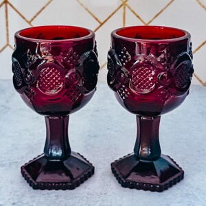 May include: Two deep red glass goblets featuring a textured geometric pattern on the bowl and a hexagonal base. The text Vintage GLASSWARE and HAND SELECTED BY A CRAFT COCKTAIL LOVER is visible at the top and bottom of the image frame.