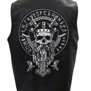 May include: Black leather vest featuring a large white Viking skull patch on the back. The patch includes a horned helmet, axes, runes, and a hammer symbol. Two smaller bird patches are below the main design.