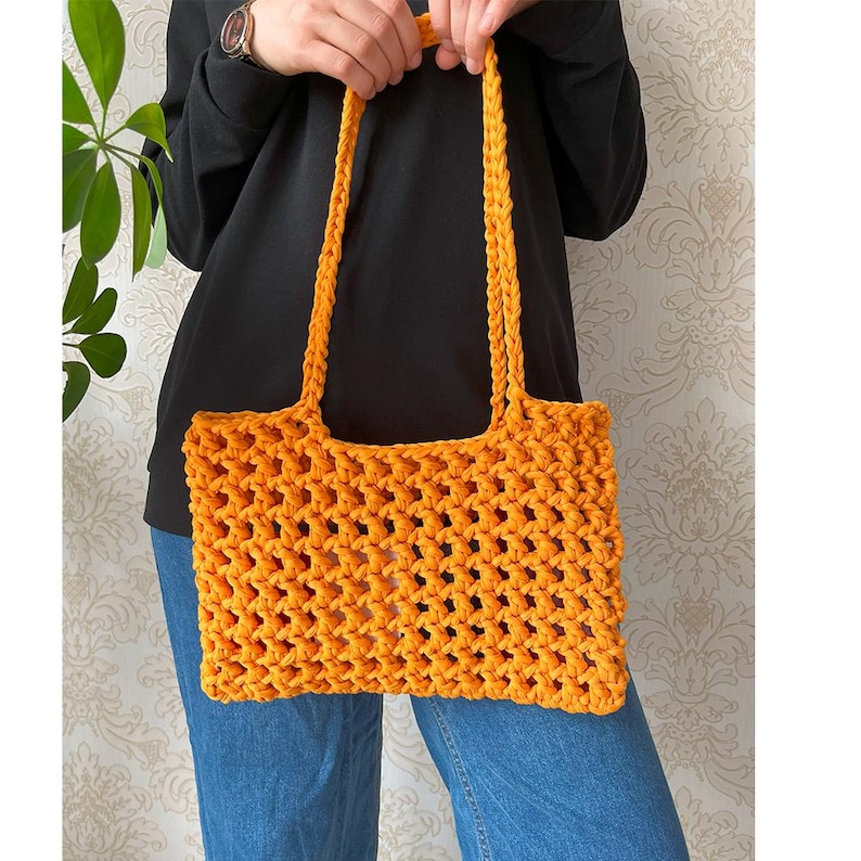 May include: A bright orange crocheted tote bag with a wide, open top and a thick, woven strap.