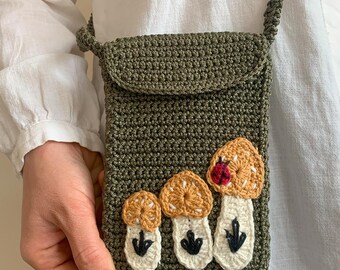 May include: A green crocheted crossbody bag with a flap closure and a crocheted design of mushrooms with red ladybugs on the front.