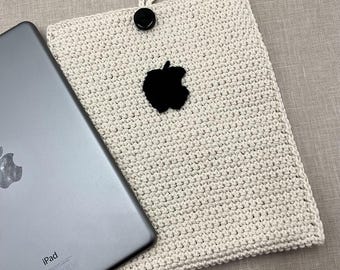Op de afbeelding: Een witte gehaakte iPad-hoes met een zwart Apple-logo. De hoes is gemaakt met een textuur-steek en heeft een eenvoudig ontwerp.