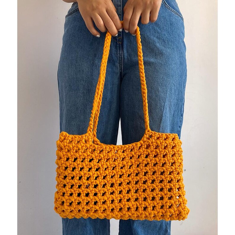 May include: A bright yellow crocheted tote bag with a wide, open top and thick straps. The bag is made of a chunky yarn and has a loose, open weave.