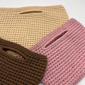 May include: Three handmade crochet bags in varying colors: beige, pink, and brown. Each bag features a rectangular shape with a handle opening. The bags are made with a thick, textured yarn, showcasing the detailed crochet work.
