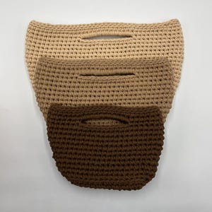 May include: Three stacked crochet bags with integrated handles, arranged in a gradient of color from light beige at the top, to medium tan in the middle, and dark brown at the bottom, each featuring a consistent textured stitch pattern.