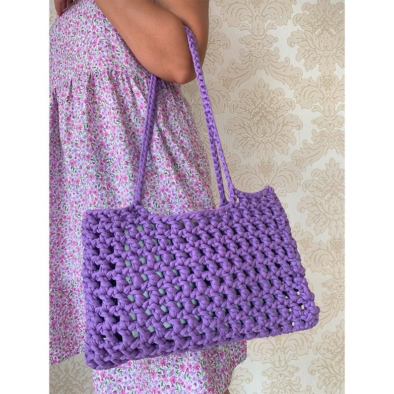 May include: A purple crocheted tote bag with a wide, open top and thick straps. The bag is made with a simple, open stitch pattern.