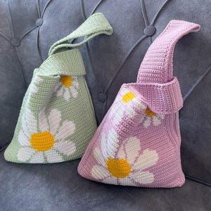 May include: Two crocheted bags with daisy flower designs. One bag is green and the other is purple.
