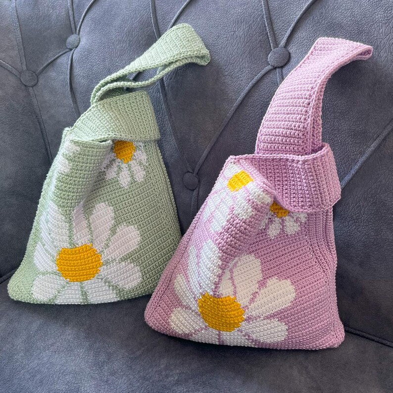 May include: Two crocheted bags with daisy flower designs. One bag is green and the other is purple.
