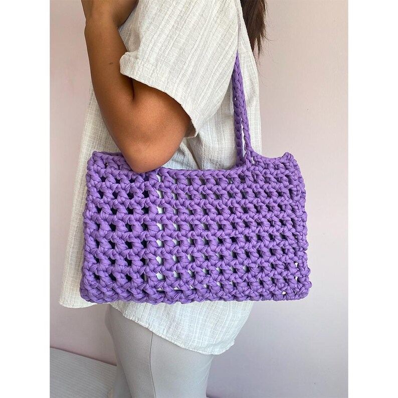 May include: A purple crocheted tote bag with a wide, open top and thick straps. The bag is made of a single strand of yarn and has a simple, geometric design.