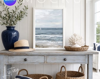 May include: A coastal-themed vignette featuring a framed seascape painting, a straw hat with a navy band, a navy blue vase with greenery, and a decorative coral piece. The scene is set on a light blue console table with woven baskets and a striped throw.