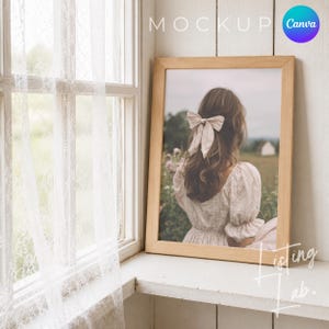 May include: A framed print featuring a woman with long brown hair and a bow, set against a field backdrop. The wooden frame rests on a white windowsill next to a lace curtain. The word "MOCKUP" is visible at the top.