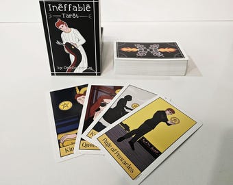May include: A black tarot card box with the text "Ineffable Tarot" and a stack of tarot cards. Several individual cards are displayed, featuring illustrations and titles like "King" and "Page of Pentacles". The cards have a white border and a yellow background.