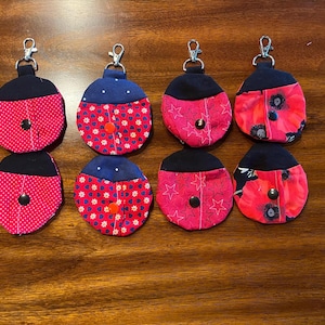 May include: Eight ladybug-themed keychains. Each keychain features a red and black design, with varying patterns including polka dots, hearts, and stars. They have a small button closure and a silver-colored clip.