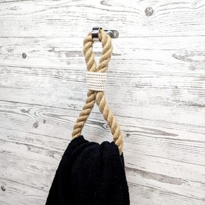 May include: A brown rope towel hook with a metal ring attached to a white wood wall. A black towel is hanging on the hook.