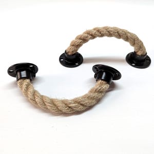 Puede incluir: Dos tiradores de cuerda de metal negro con una cuerda de yute natural. La cuerda está trenzada y tiene un aspecto rústico.