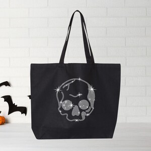 Puede incluir: Bolsa de tela negra con un dise&ntilde;o de calavera plateada brillante. La calavera tiene un dise&ntilde;o detallado con un patr&oacute;n de diamante.