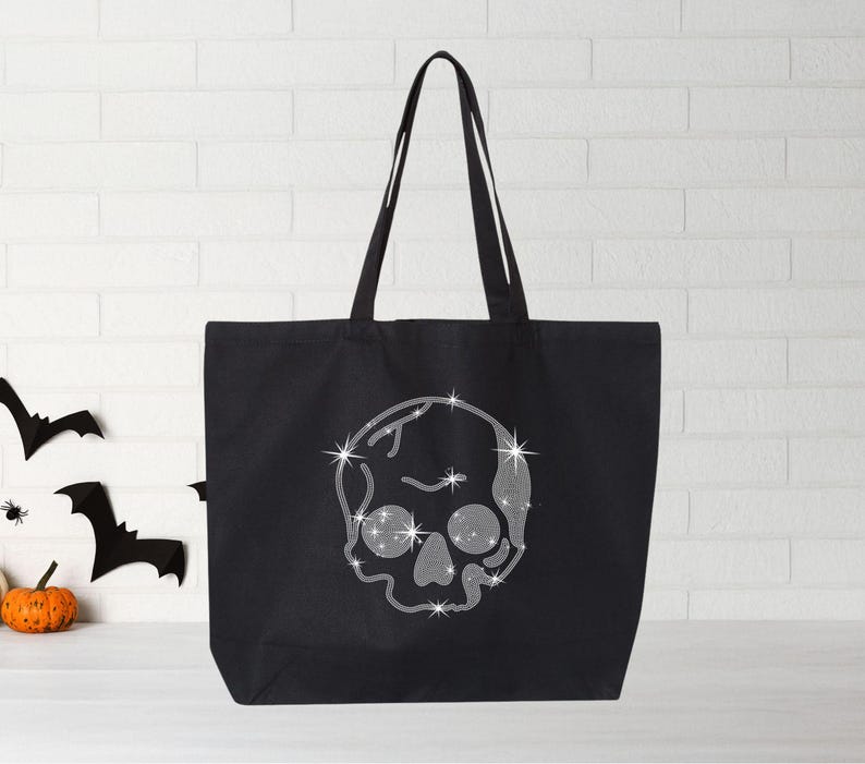 Puede incluir: Bolsa de tela negra con un dise&ntilde;o de calavera plateada brillante. La calavera tiene un dise&ntilde;o detallado con un patr&oacute;n de diamante.