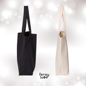 Puede incluir: Dos bolsas de tela, una negra y una blanca, con asas largas. Ambas bolsas est&aacute;n hechas de lona.