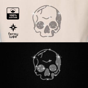 Puede incluir: Una camiseta blanca con un dise&ntilde;o de calavera de strass. La calavera est&aacute; bordeada de plata y tiene un fondo negro. El texto "feray luxe" est&aacute; impreso debajo de la calavera.